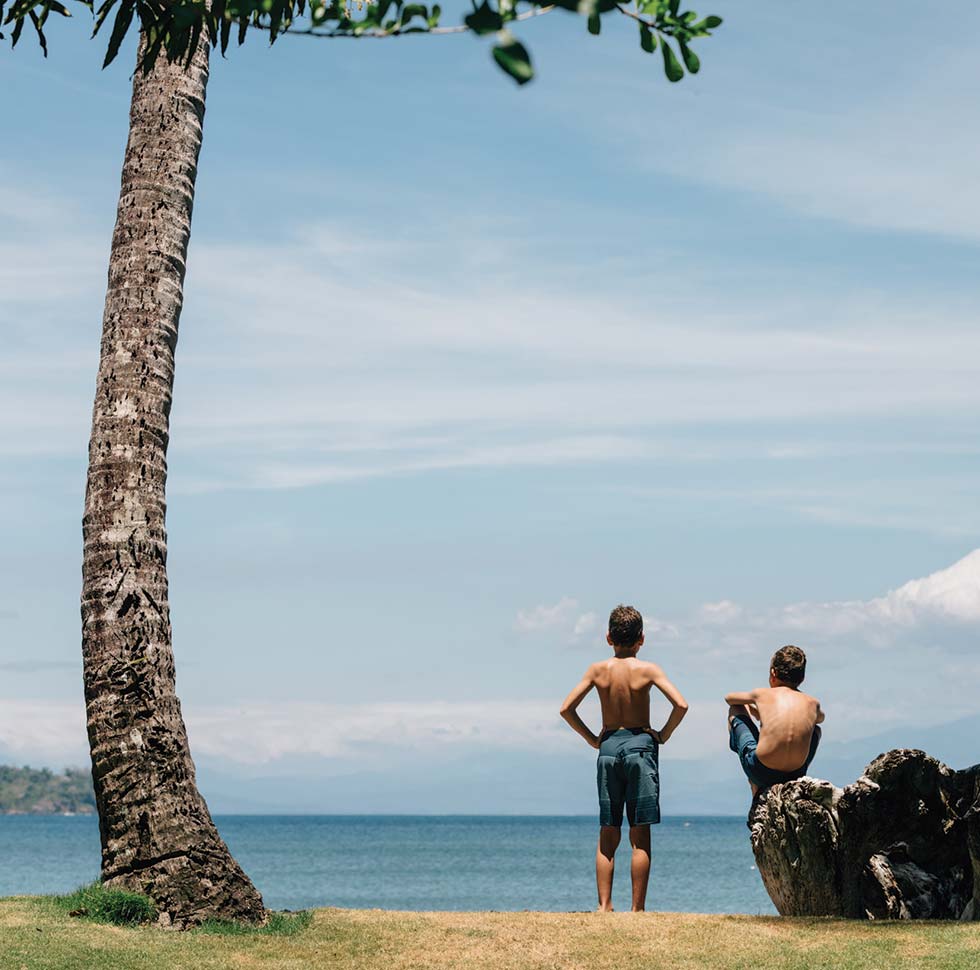 Two children rest and admire the view into the ocean from the shore of Islas Secas, a sustainable island resort off the coast of Panama | Islas Secas